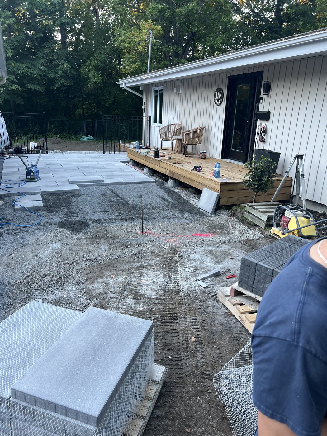 Compacted gravel base with the first course of pavers going down and stone pallets staged nearby